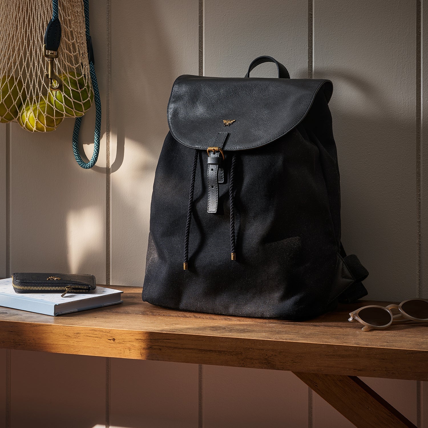 Sophie Allport's black Bees Backpack made from cotton and leather sat on a wooden bench