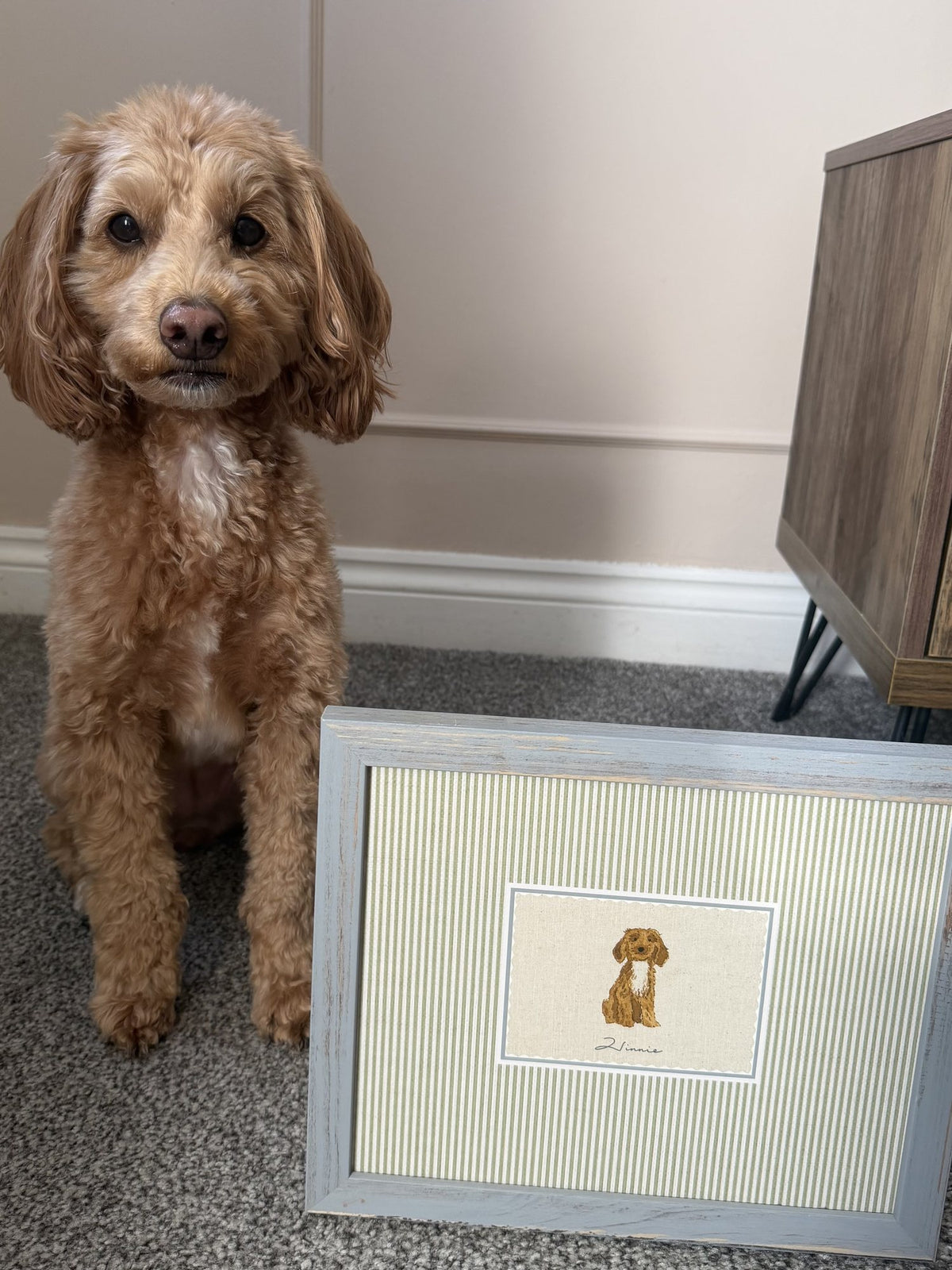 Winnie the cockapoo sitting beside a framed personalised dog print with an olive printed mount